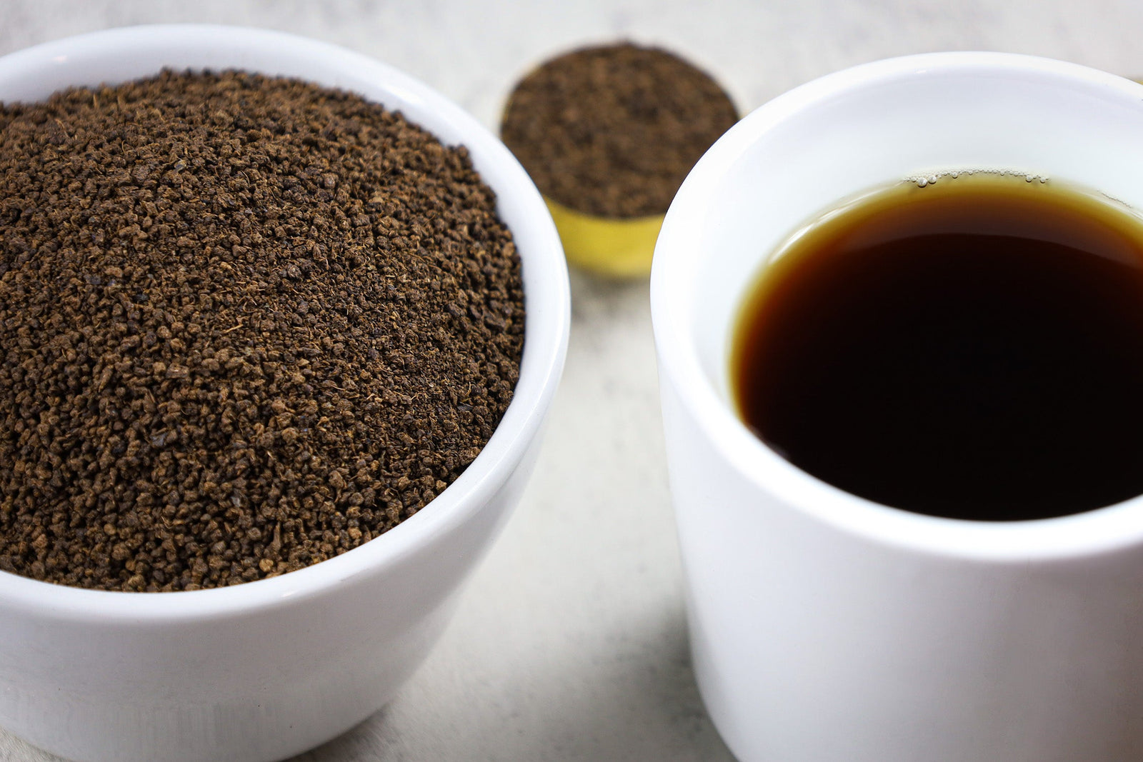 A bowl of loose leaf Decaf Irish Breakfast tea, next to a steeped cup of Decaf Irish Breakfast tea