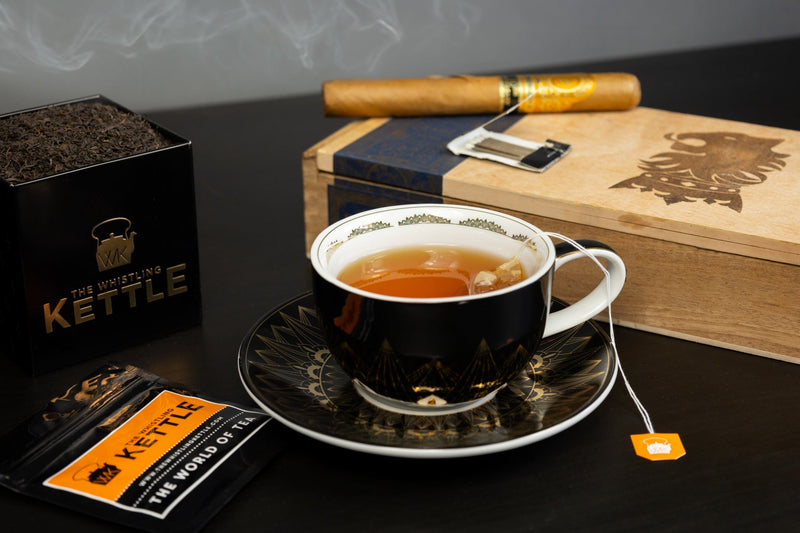 A hot cup of lapsang souchong tea next to a lit cigar