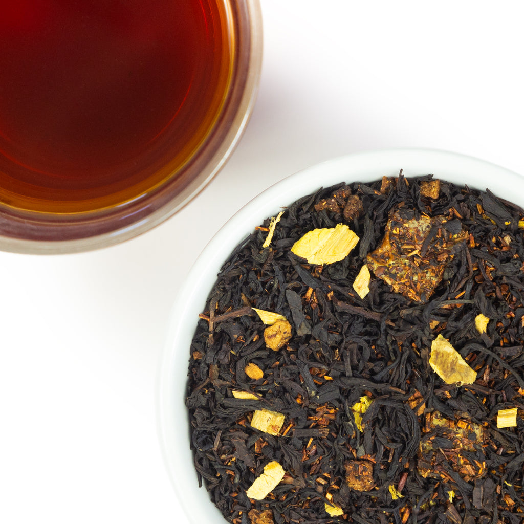 A top-down view of a bowl of Caramel Apple Bourbon tea leaves sits next to a cup of brewed tea