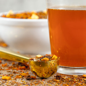 Glass of brewed Carrot Cake next to Gold Tea Scoop filled with Carrot Cake loose leaf tea.