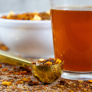 Glass of brewed Carrot Cake next to Gold Tea Scoop filled with Carrot Cake loose leaf tea.