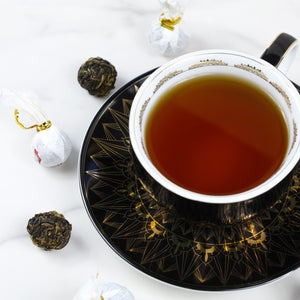 Cup & Saucer filled with brewed Black Dragon Pearls next to Black Dragon Pearls loose leaf tea.