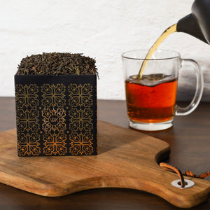 Pouring brewed English Evening into glass next to Tea Tin filled with English Evening loose leaf tea.