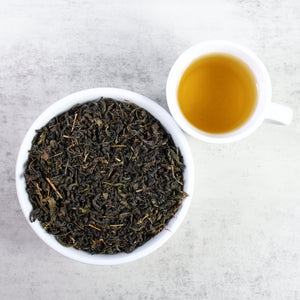 Cup of brewed Japanese Oolong tea next to bowl of Japanese Oolong tea leaves.