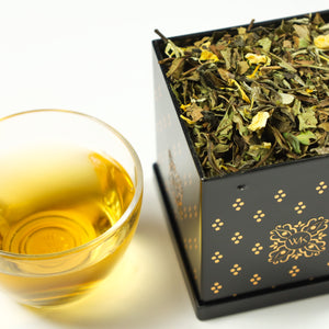 Glass of brewed Mango Pear White next to Tea Tin filled with Mango Pear White loose leaf tea.