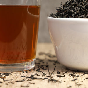 Glass of Secret Village tea next to bowl of Secret Village tea leaves.