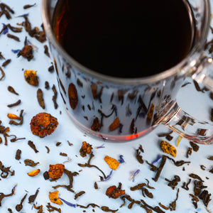 Glass of Pu-erh Superfruit tea next to Pu-erh Superfruit tea leaves.